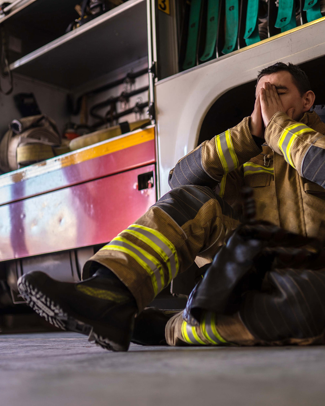 a firefighter sitting next to a fire engine covering face with hands